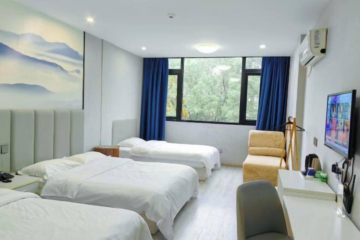 Habitación de hotel con tres camas, un escritorio, una silla, un televisor y una ventana con cortinas.
