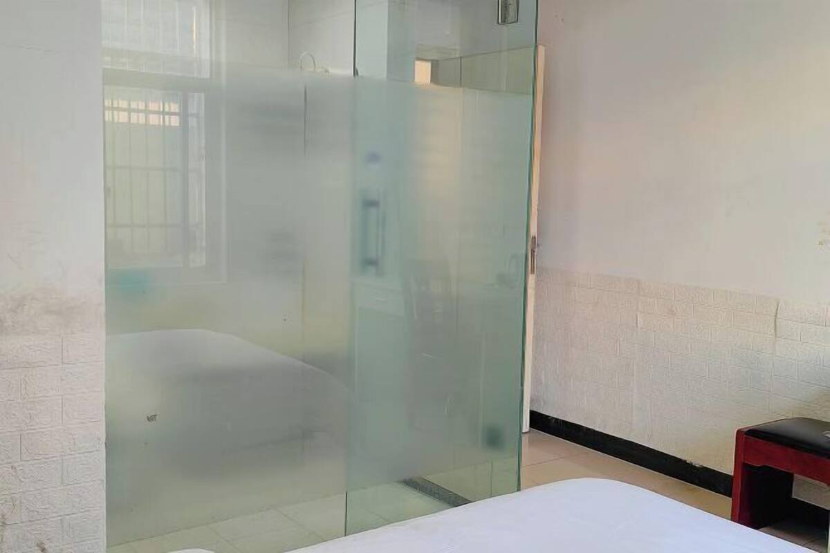 Una habitación con cama, un separador de vidrio y una pequeña mesa.