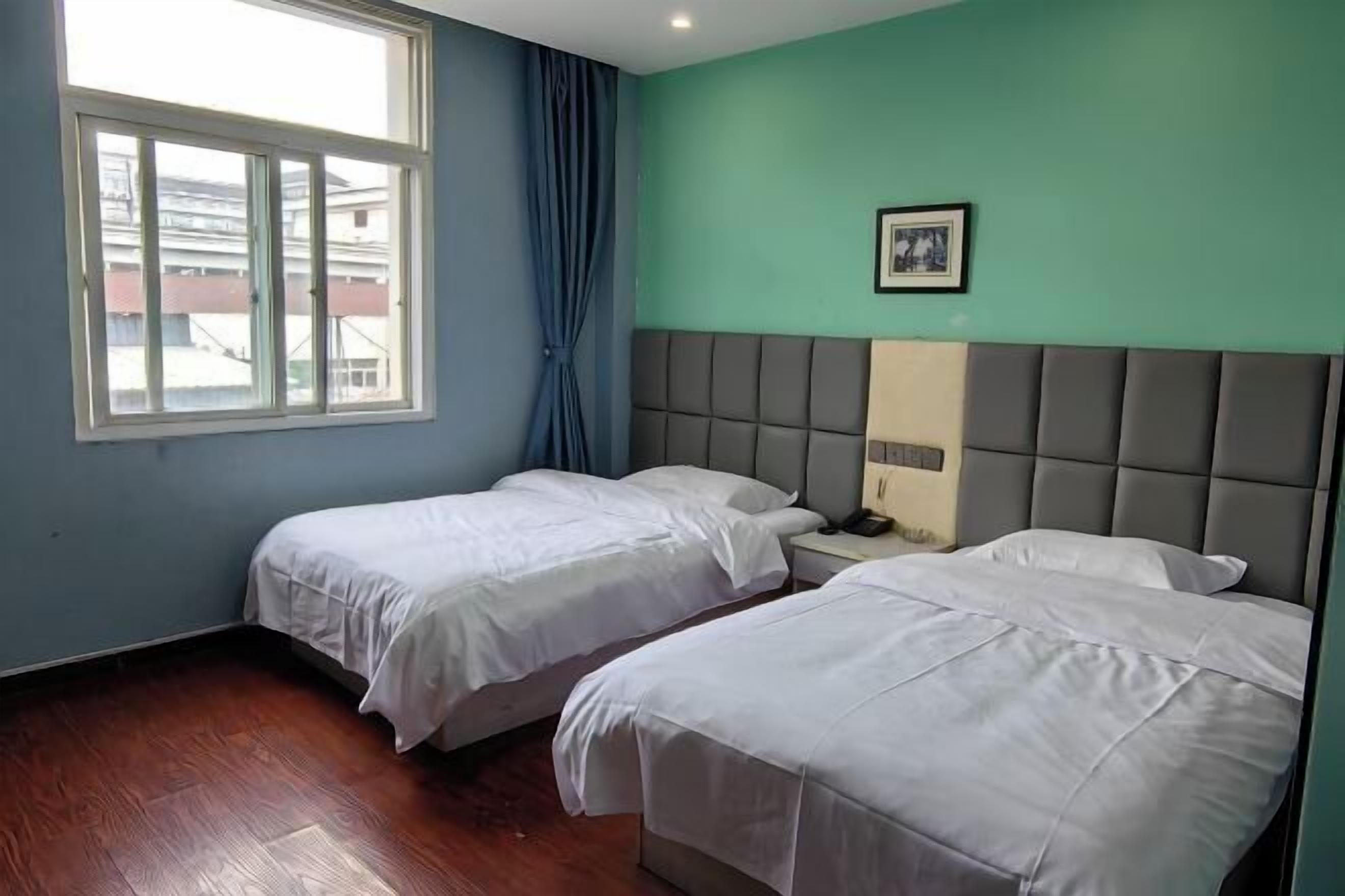 Een kamer met twee bedden, een raam met gordijnen, een hoofdbord en een ingelijst beeld aan de muur.