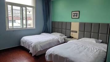 Een kamer met twee bedden, een raam met gordijnen, een hoofdbord en een ingelijst beeld aan de muur.