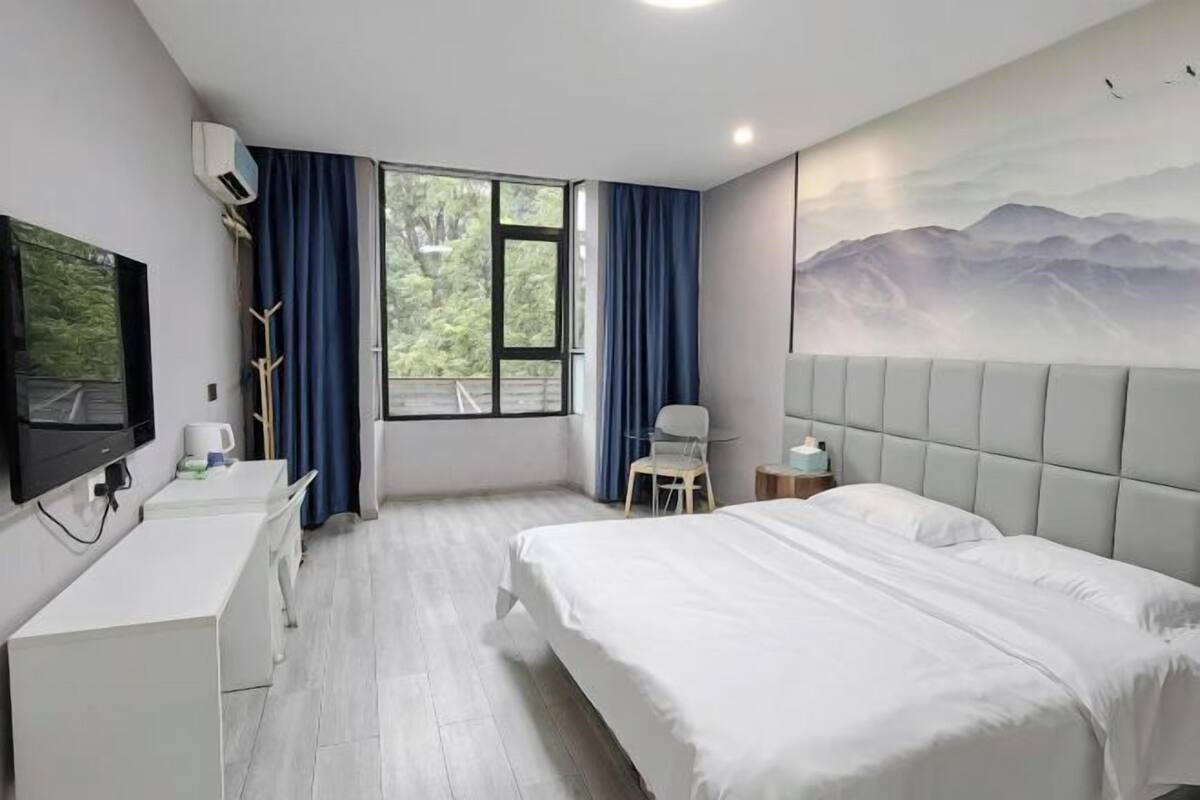 Una habitación de hotel con cama, escritorio, silla, televisor y ventana con cortinas.
