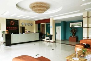 Un espace d’accueil d’hôtel comprenant un comptoir de réception, des chaises, un lustre et un bureau d’accueil.