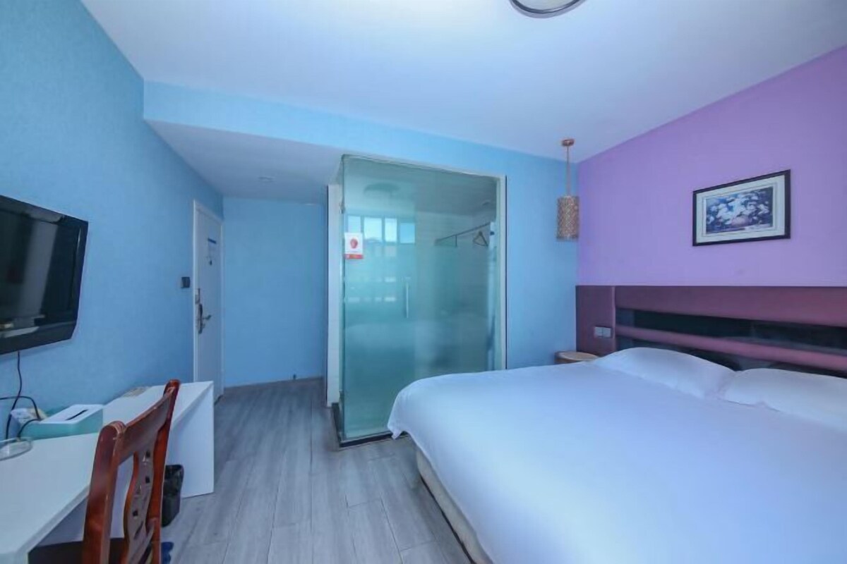 Une chambre à coucher comprenant un lit, un bureau, une chaise, un téléviseur et une cabine de douche en verre.