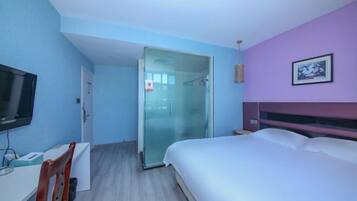 Een slaapkamer met een bed, een bureau, een stoel, een televisie en een douchecabine met glazen wanden.