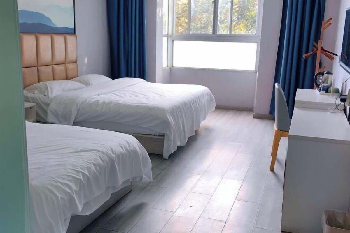 Une chambre d’hôtel avec deux lits, un bureau et une fenêtre avec des rideaux.