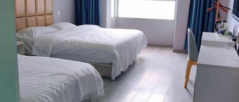 A hotel room with two beds, a desk, and a window with curtains.