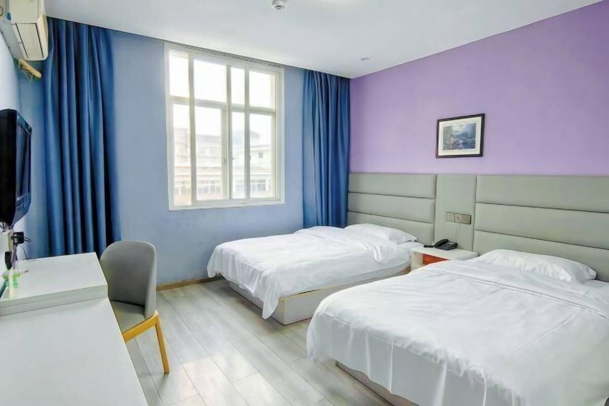 Habitación de hotel con dos camas, un escritorio, una silla y una ventana con cortinas.
