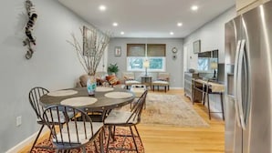 A modern kitchen with a dining area, featuring a round table with chairs, a refrigerator, and a window providing natural light.