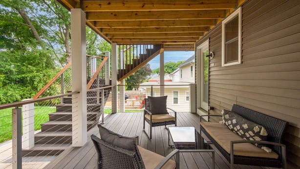 A covered deck with a staircase, outdoor furniture, and a view of neighboring houses.