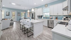 A modern kitchen with white cabinetry, a central island with bar stools, stainless steel appliances, and a blue accent wall.