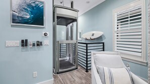 A room with a modern design, featuring a ceiling fan, a mounted artwork of a wave, a surfboard, and a bed with a striped pillow.