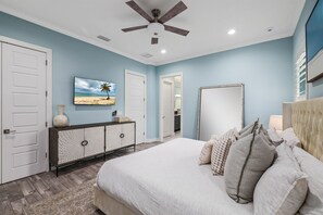 A bedroom with a bed, a ceiling fan, a TV, a dresser, and a mirror. - Ocean View Bliss | Steps to Beach | Golf Cart Perk (Jacksonville Beach)