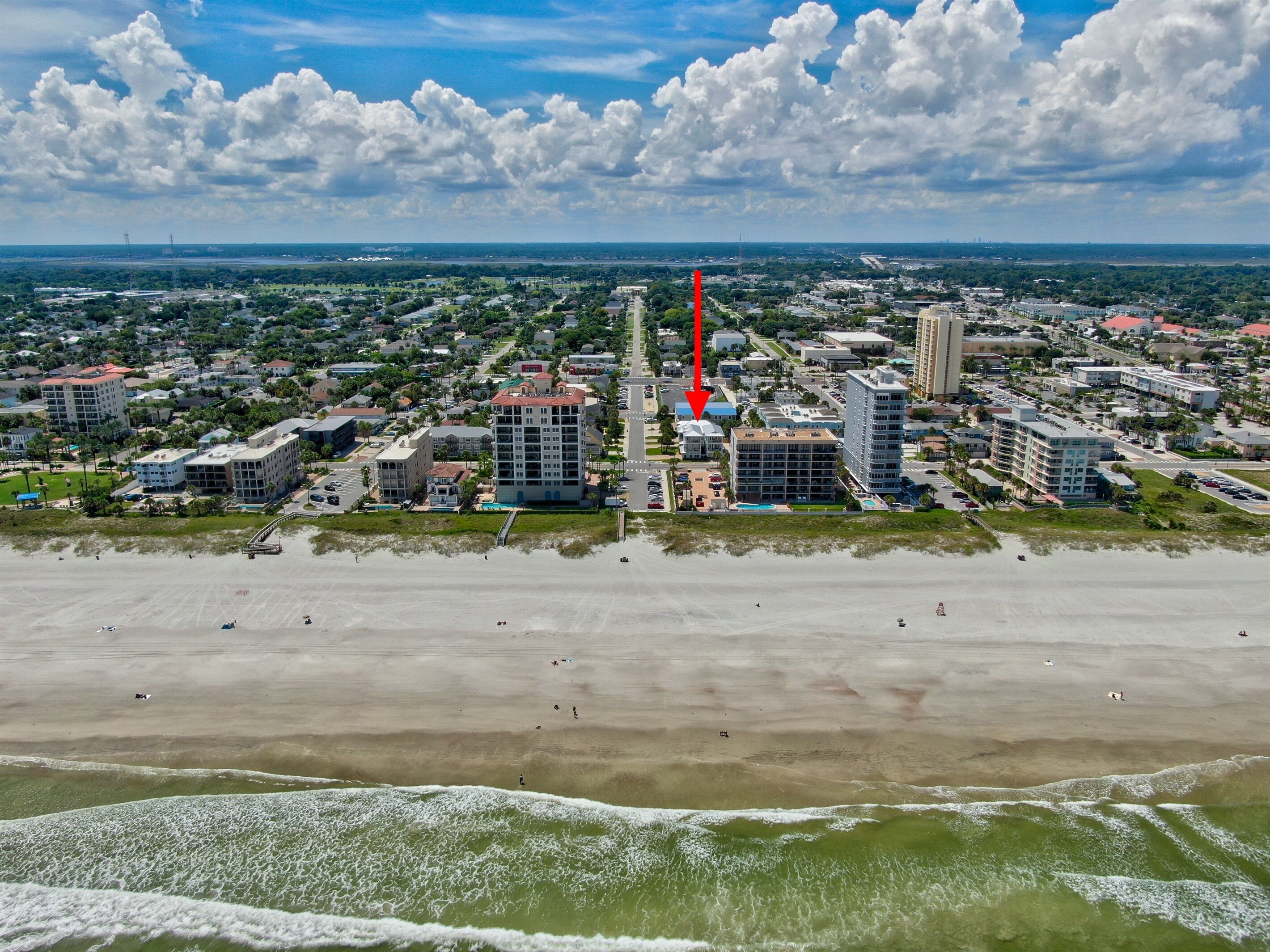 A coastal cityscape with a prominent hotel featuring multiple floors and a rooftop pool.
