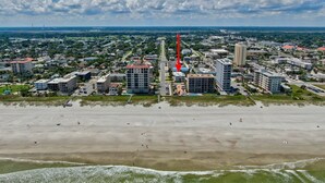A coastal cityscape with a prominent hotel featuring multiple floors and a rooftop pool.