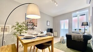 A modern living room with a dining area, featuring a wooden dining table, chairs, a sofa, and a large lamp. - Lavapies - One-bedroom Apartment (MADRID)