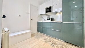 A modern kitchen with white and teal cabinets, a microwave, and a sink. - Lavapies - One-bedroom Apartment (MADRID)