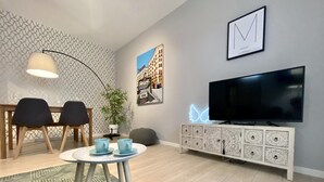 A modern living room with a round coffee table, two chairs, a TV, and a decorative cabinet. - Lavapies - One-bedroom Apartment (MADRID)