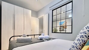 A hotel room with a bed, a window with a view of buildings, a wardrobe, and a door. - Lavapies - One-bedroom Apartment (MADRID)