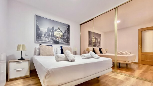 Ein modernes Schlafzimmer mit einem großen Bett, einem Nachttisch, einem Spiegel und einem Stadtbild an der Wand.