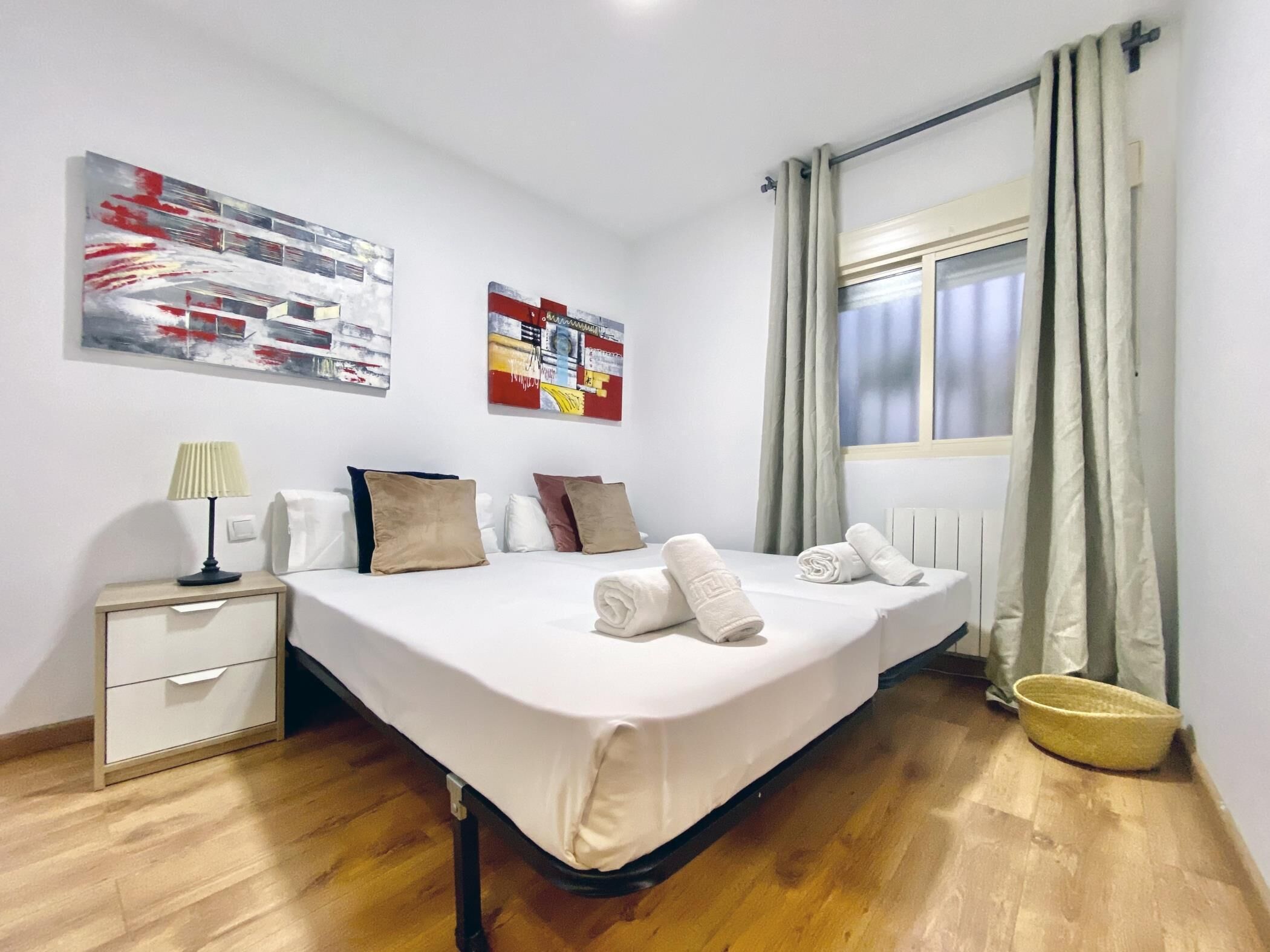 Une chambre d’hôtel avec un lit, une table de chevet, une lampe, une fenêtre avec des rideaux et des œuvres d’art accrochées aux murs.