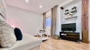 Ein Wohnzimmer mit einer Couch, einem kleinen weißen Tisch, einem Fernseher auf einem Holzgestell und einer Heizung.