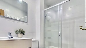 Ein modernes Badezimmer mit Duschkabine aus Glas, Toilette in Weiß und Waschbecken mit Spiegel darüber.
