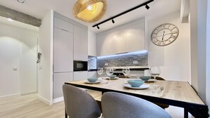 A modern kitchen with a dining area, featuring a wooden table, grey chairs, and a large wall clock.