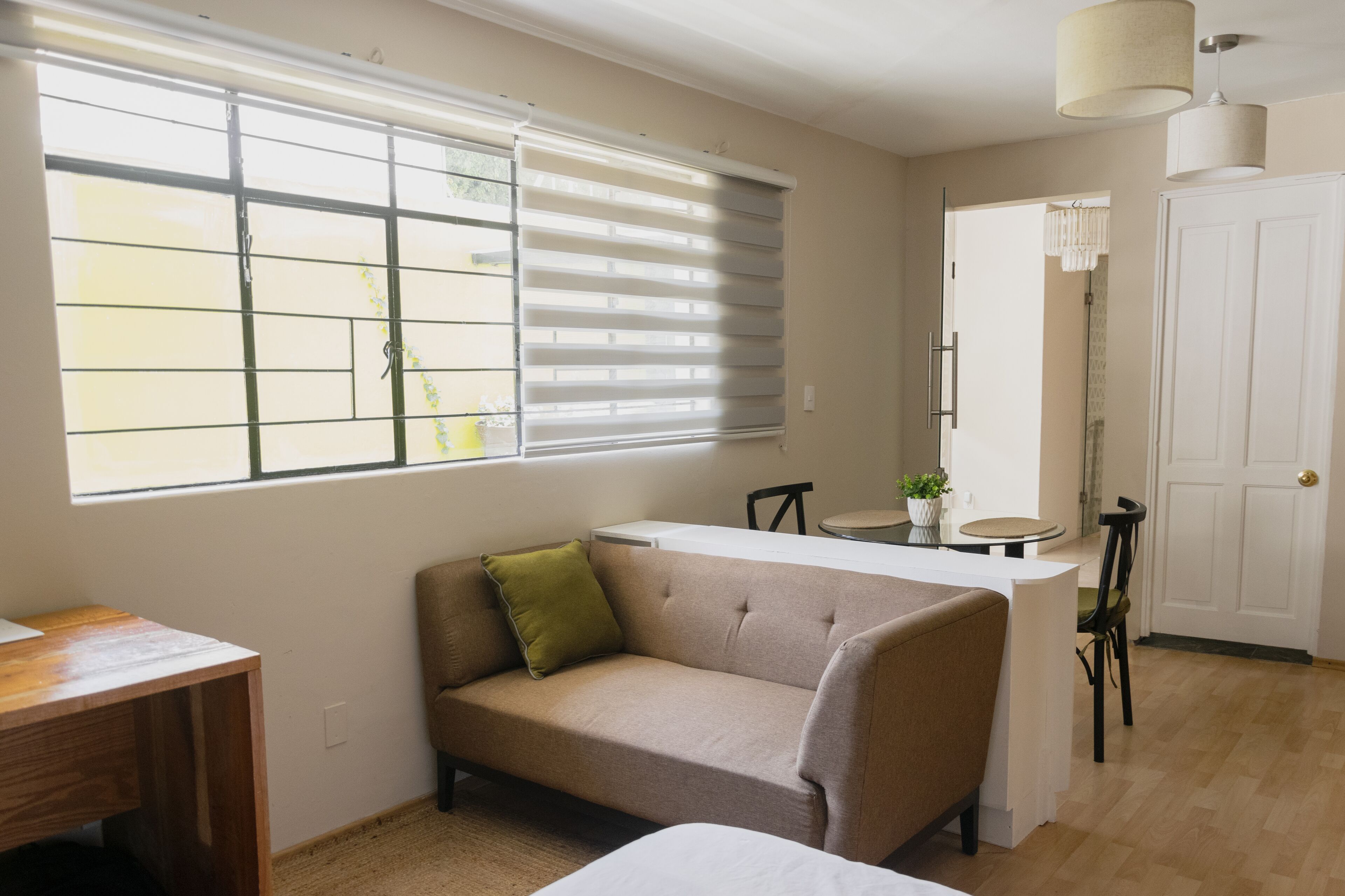 A room with a sofa, a small table, a chair, a window with blinds, a door, and a light fixture.