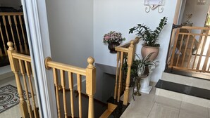 Una escalera de madera con barandilla, una planta en maceta y piso de baldosas.