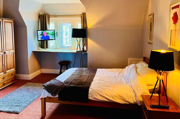 Relax in this inviting room with a comfortable bed, bedside table, and TV, plus a wardrobe and window with curtains.