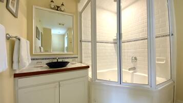 A bathroom with a white sink, a mirror, and a shower enclosure.