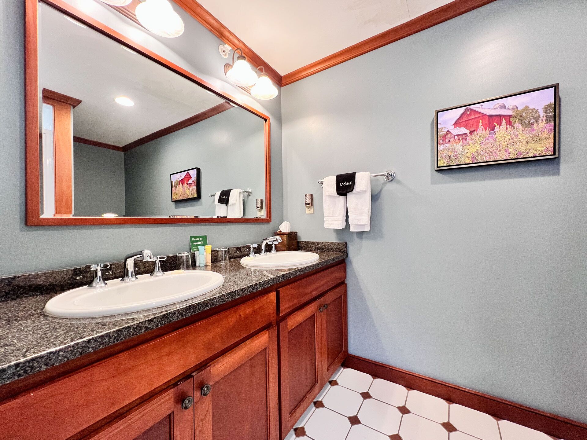 A bathroom with two sinks, a large mirror, and a framed picture on the wall.