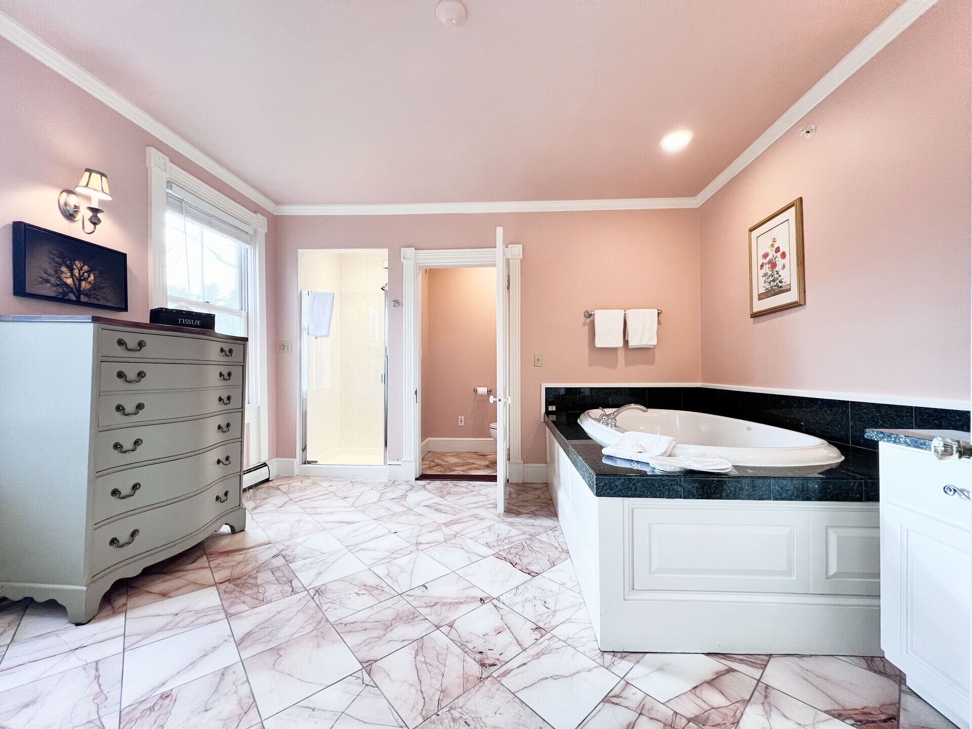 A bathroom with a marble floor, a bathtub, a vanity, and a tissue box on a cabinet.