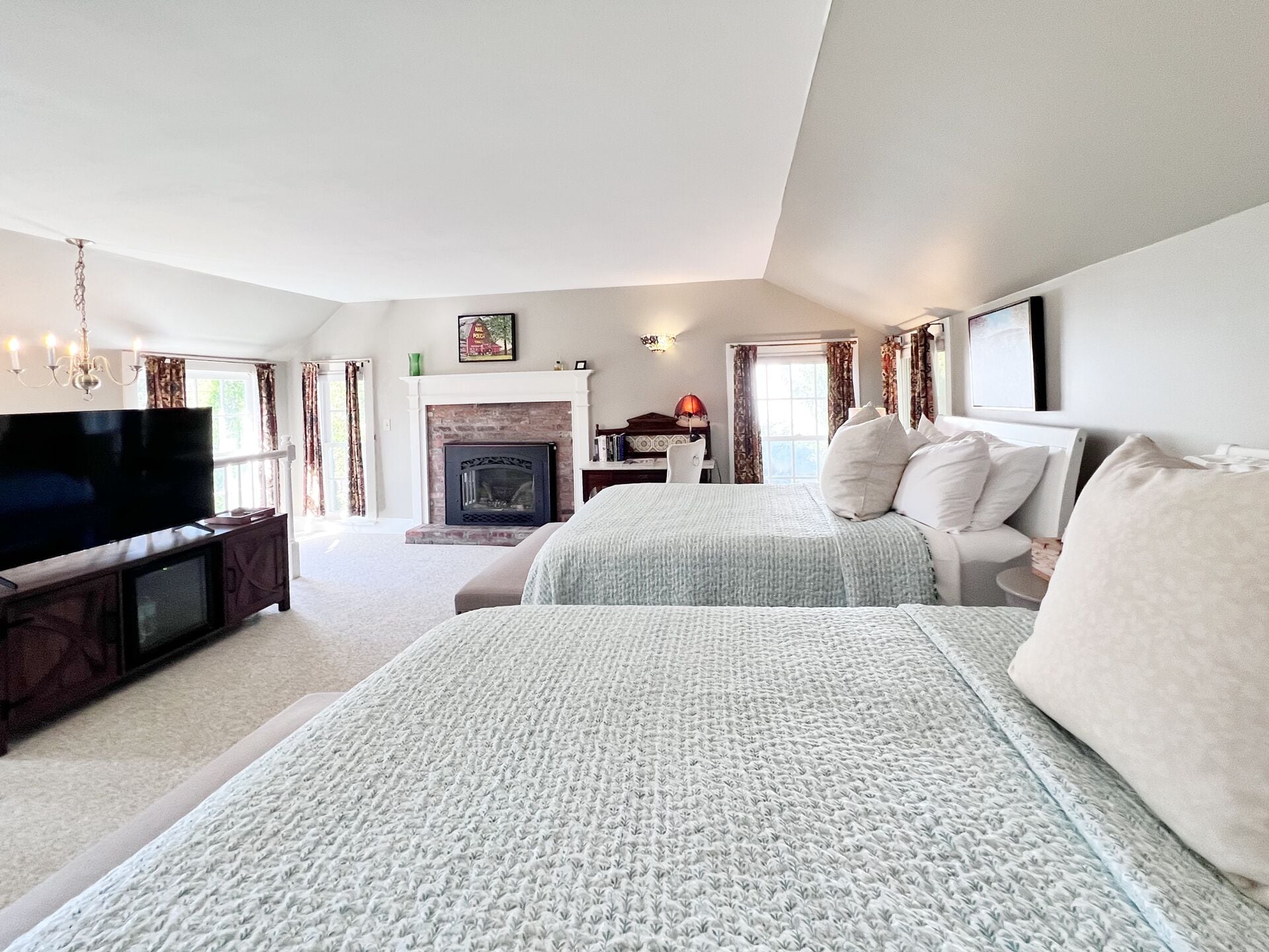 A bedroom with a large bed, a television, a fireplace, and a desk with a chair.