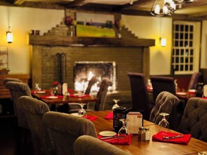 A restaurant with a brick fireplace, wooden tables, and red napkins. - Four Columns Inn (Newfane)