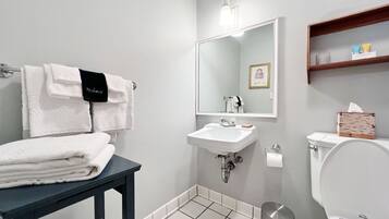 Une salle de bain équipée d’un lavabo, d’un miroir, de toilettes et d’une petite table sur laquelle sont posées des serviettes.