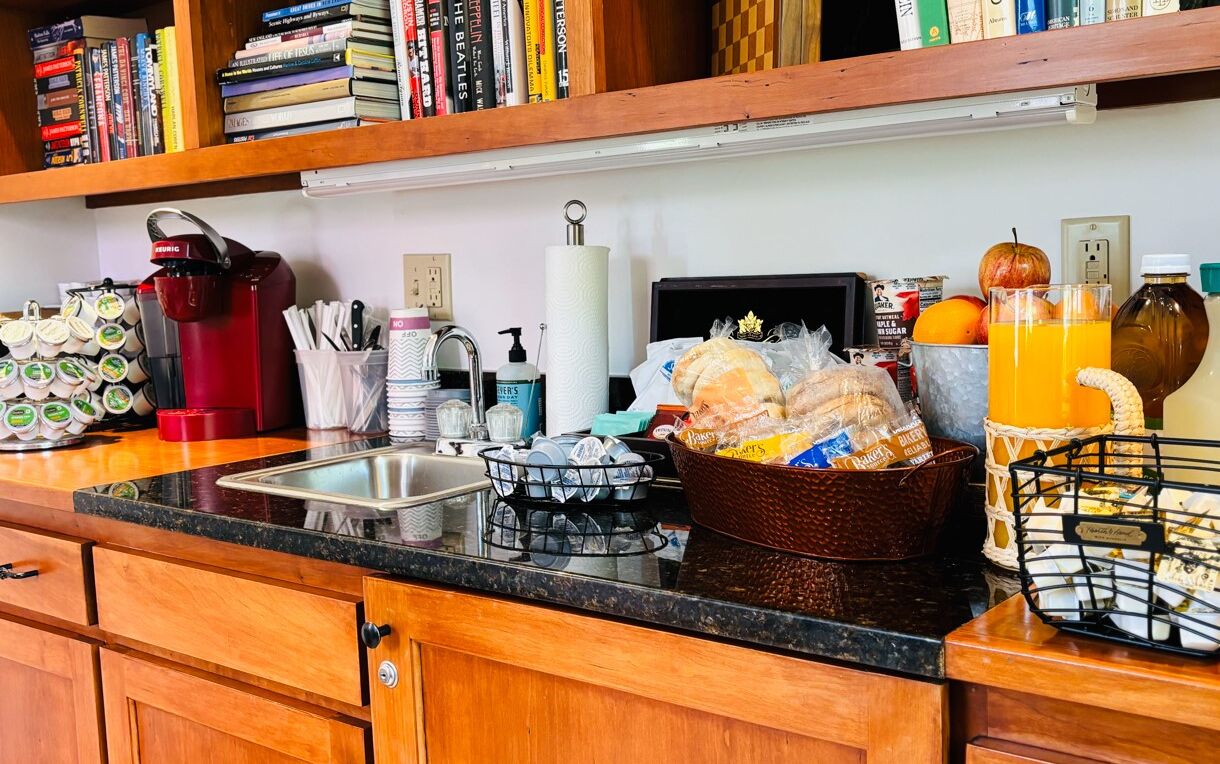 Une cuisine avec des meubles de rangement en bois, une machine à café, un évier et divers produits alimentaires.