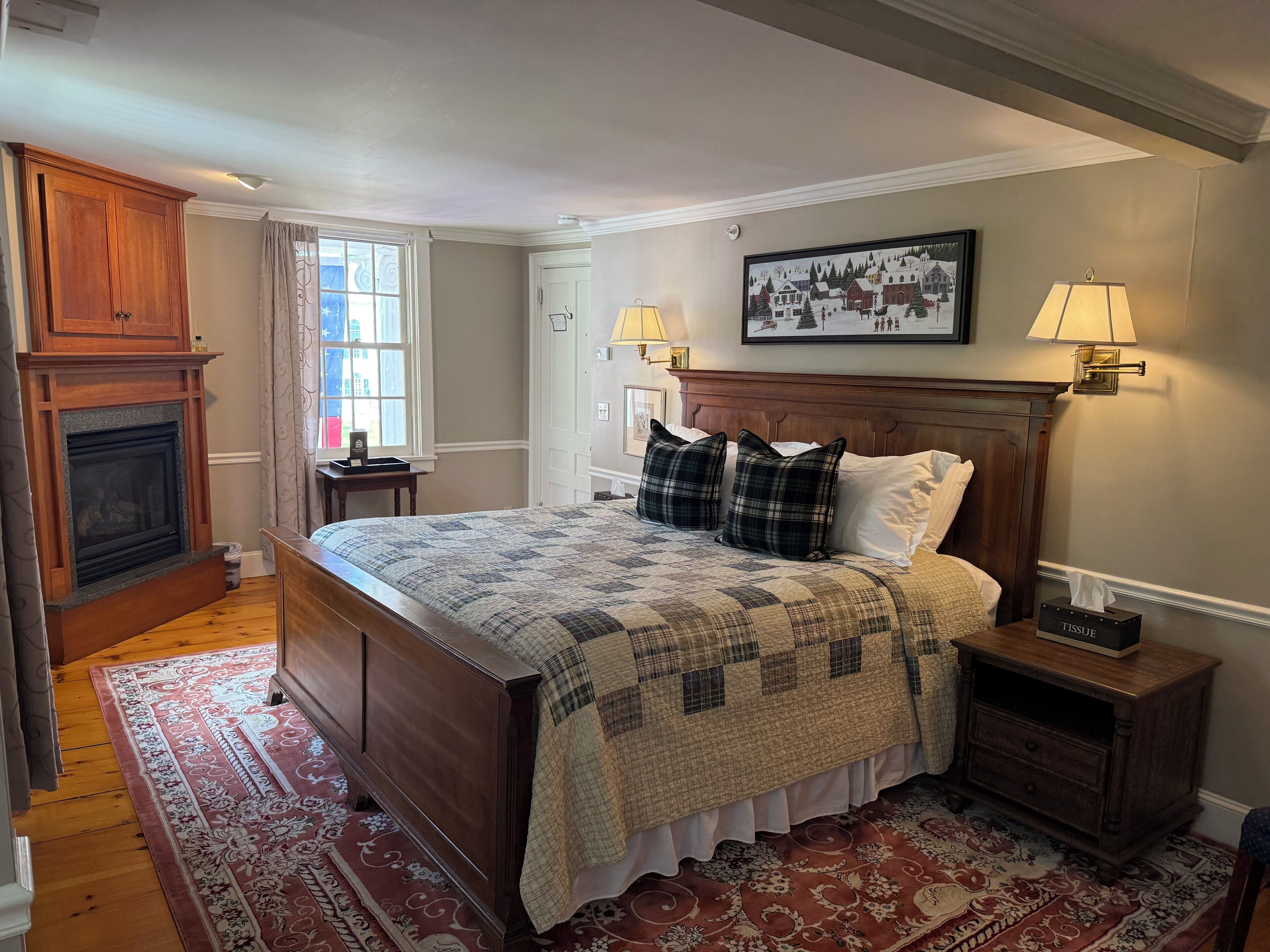 A bedroom with a large bed, a fireplace, a rug, and a framed picture on the wall.