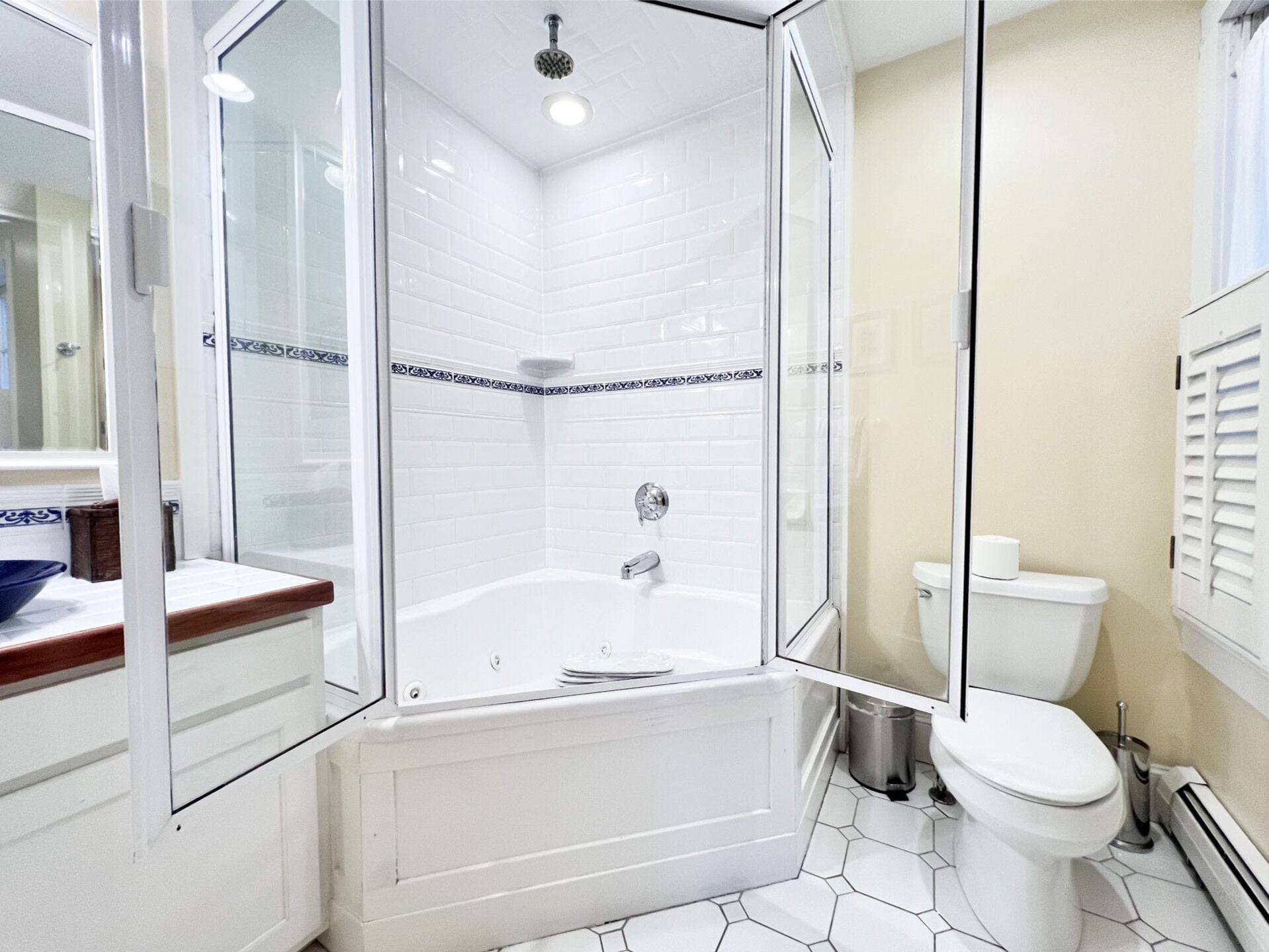 A modern bathroom with a glass-enclosed shower, white tiled walls, a white toilet, and a wooden vanity.
