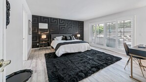 Une chambre moderne avec un grand lit, un tapis noir, un bureau avec une chaise et une vue sur l’extérieur grâce à de grandes fenêtres.