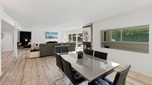 Un salon moderne comprenant un coin repas, une cheminée et une grande fenêtre donnant sur un paysage verdoyant.