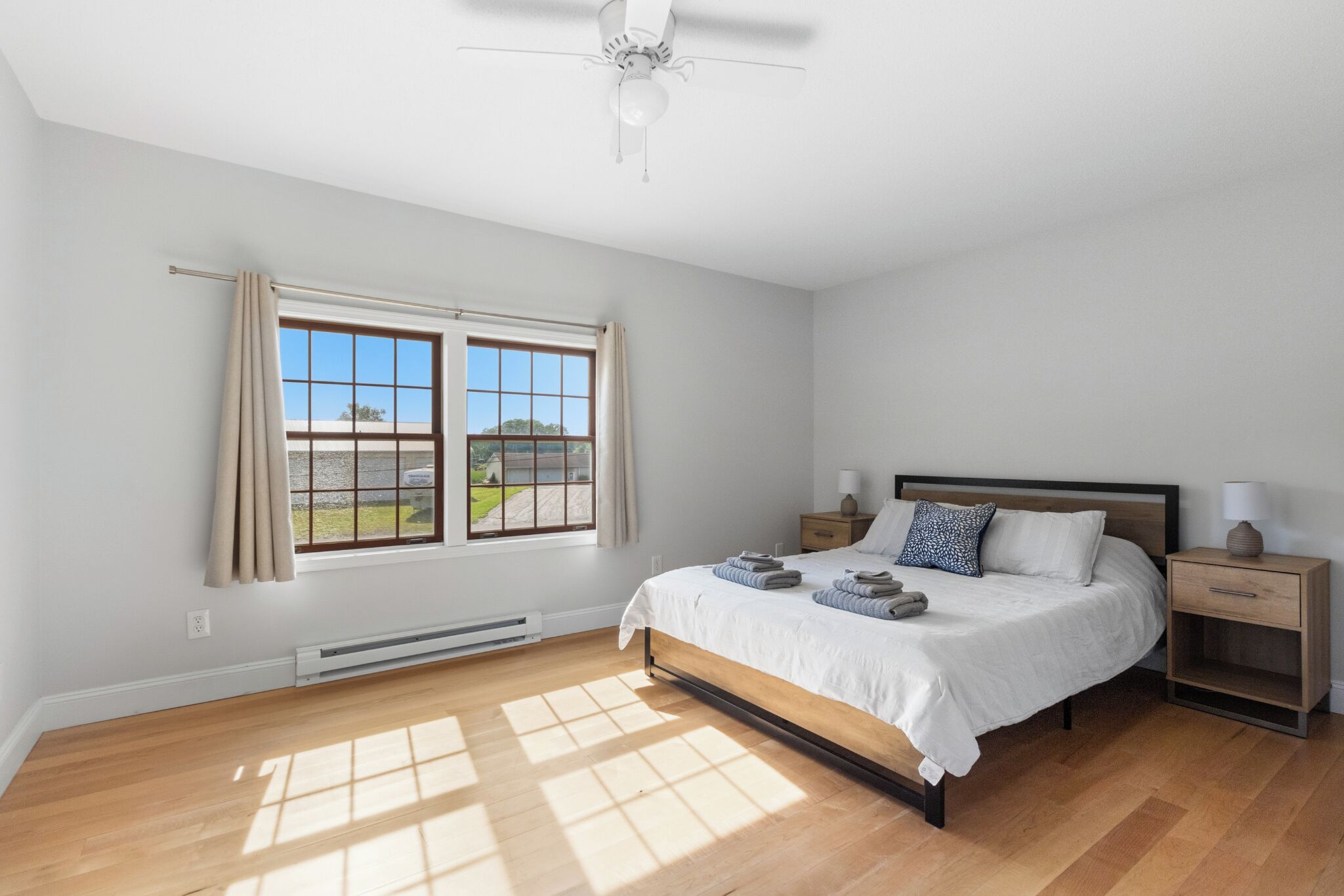 Une chambre à coucher avec un lit, des tables de chevet, un ventilateur de plafond et une fenêtre avec des rideaux.