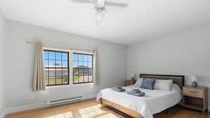 Une chambre à coucher avec un lit, des tables de chevet, un ventilateur de plafond et une fenêtre avec des rideaux.