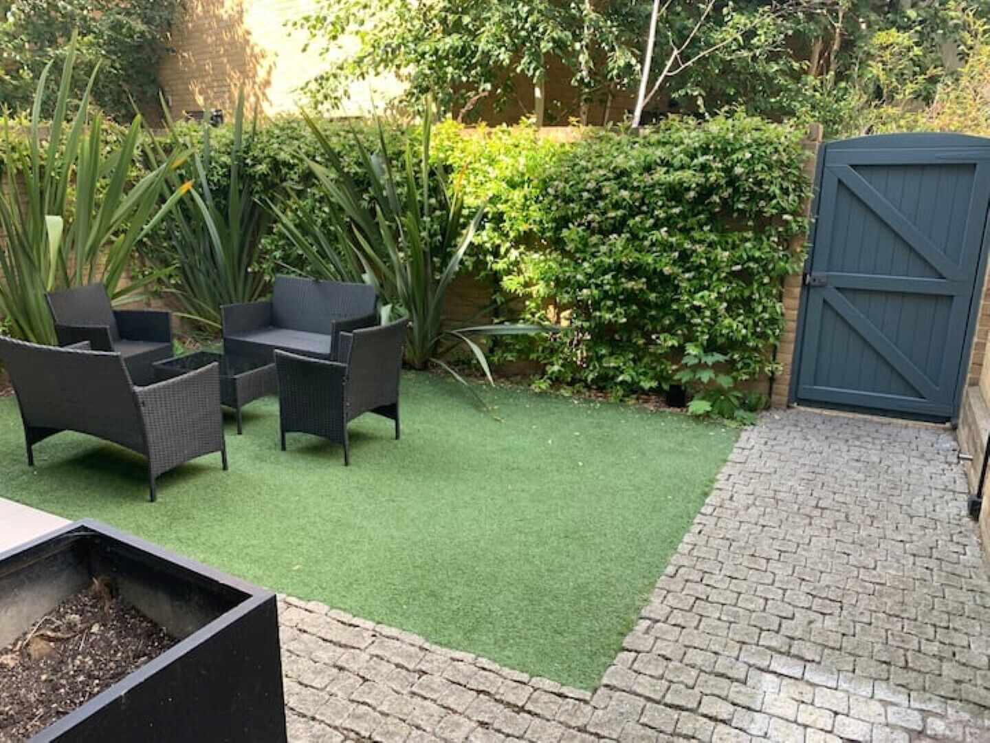 Un espace patio aménagé avec du mobilier d’extérieur, une pelouse verdoyante, un chemin en briques et un portail sombre.