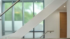 Un intérieur moderne avec un escalier en verre, une porte en bois et une vue sur la verdure environnante.