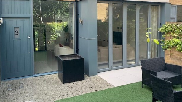 Un espace patio extérieur moderne, doté d’une porte-fenêtre coulissante donnant sur une pièce, d’un petit coin salon avec un canapé et une table basse, et d’une plante en pot.