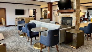 A hotel lobby with a stone fireplace, a flat-screen TV, a seating area with sofas and chairs, and a dining area with a table and chairs. - Spacious Accessible Studio w/ Walk-In Shower (Oconomowoc)