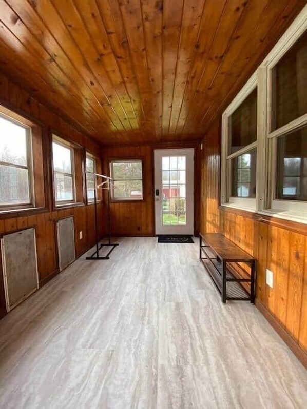 Una habitación con paredes y techo de madera, ventanas amplias y una puerta.