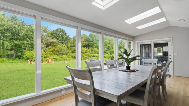 A dining area with a large table, chairs, and a view of a green lawn.