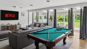 A living room with a pool table, a sofa, and a TV displaying 'NETFLIX'.